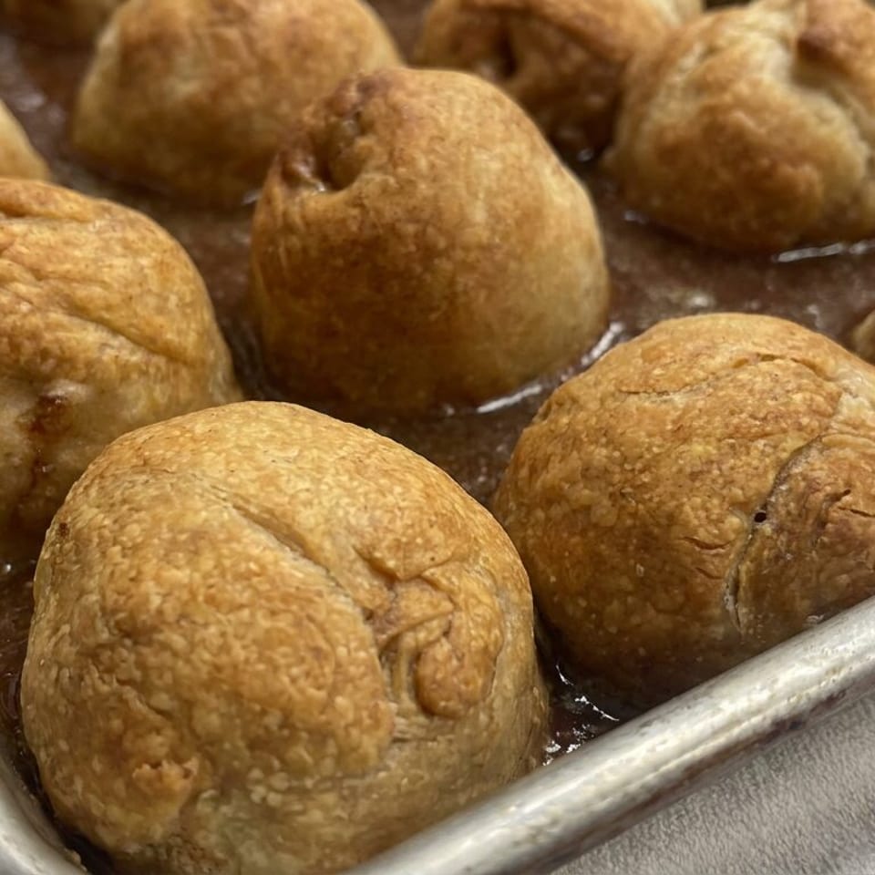 Golden-brown round pastries bake in oil inside a metal tray.