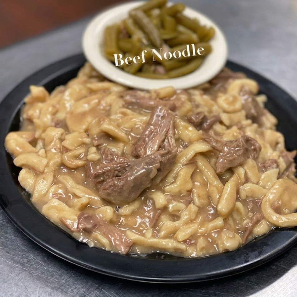 Plate of beef noodles in creamy sauce, topped with sliced beef and accompanied by green beans.